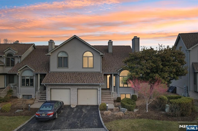 view of front facade featuring a garage, a chimney, driveway, and roof with shingles