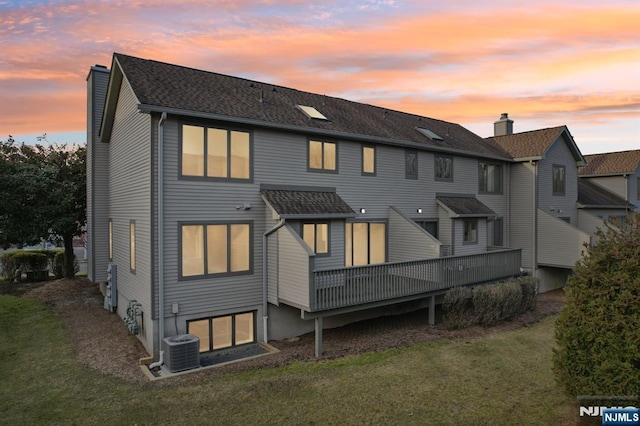 back of property at dusk featuring a lawn, cooling unit, a chimney, and a deck