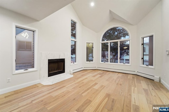 unfurnished living room featuring wood finished floors, baseboards, a high end fireplace, vaulted ceiling, and baseboard heating