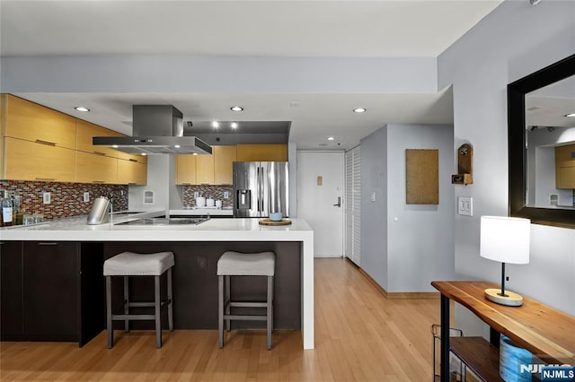 kitchen featuring island exhaust hood, a kitchen breakfast bar, stainless steel refrigerator with ice dispenser, and light countertops