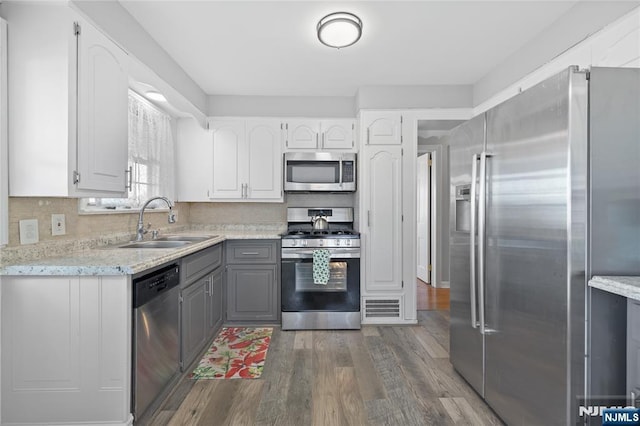 kitchen featuring gray cabinets, a sink, appliances with stainless steel finishes, decorative backsplash, and dark wood-style flooring