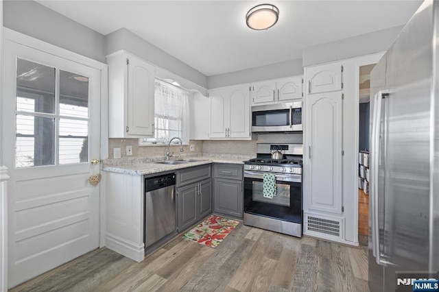 kitchen with tasteful backsplash, gray cabinetry, light wood-style flooring, appliances with stainless steel finishes, and a sink