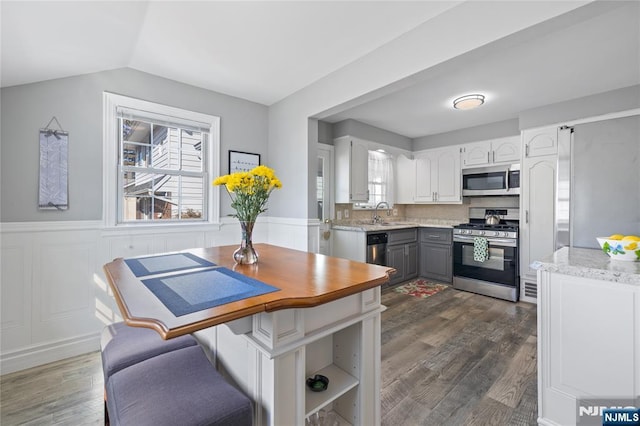 kitchen featuring a wainscoted wall, appliances with stainless steel finishes, white cabinetry, and dark wood-style flooring