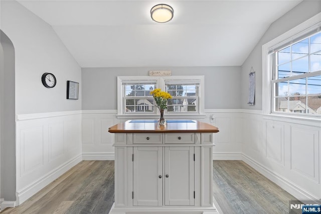 kitchen with vaulted ceiling, light wood-style flooring, wainscoting, arched walkways, and white cabinets