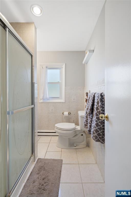 full bath featuring tile patterned floors, toilet, a shower stall, and a baseboard radiator