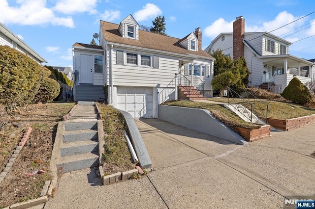 new england style home with concrete driveway, an attached garage, and a shingled roof