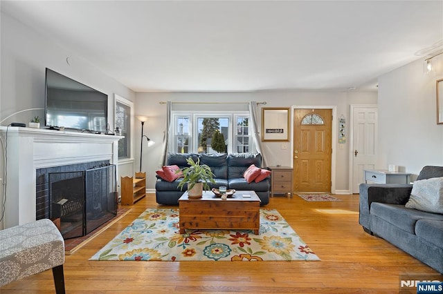 living room with a fireplace with flush hearth, baseboards, and light wood-style floors