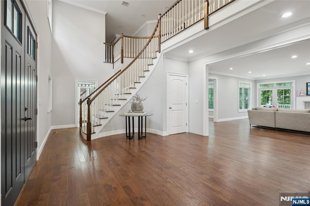 foyer entrance featuring ornamental molding, hardwood / wood-style flooring, baseboards, a towering ceiling, and stairs