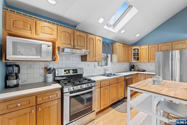 kitchen with lofted ceiling, under cabinet range hood, a sink, light countertops, and appliances with stainless steel finishes