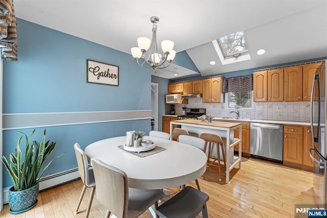 dining room featuring light wood-type flooring, a baseboard radiator, a notable chandelier, and lofted ceiling with skylight