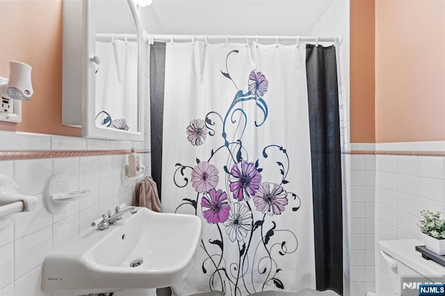 full bathroom with wainscoting, toilet, a sink, shower / bath combo with shower curtain, and tile walls