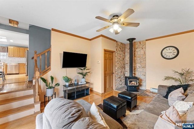 living room featuring a baseboard radiator, stairway, ornamental molding, a wood stove, and light wood-type flooring