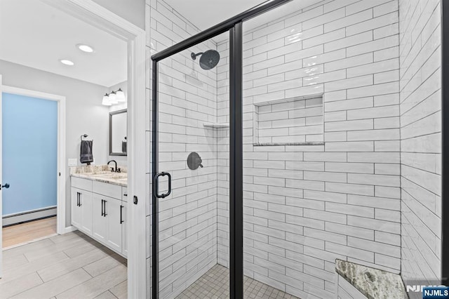 full bathroom with wood finished floors, baseboard heating, a shower stall, and vanity