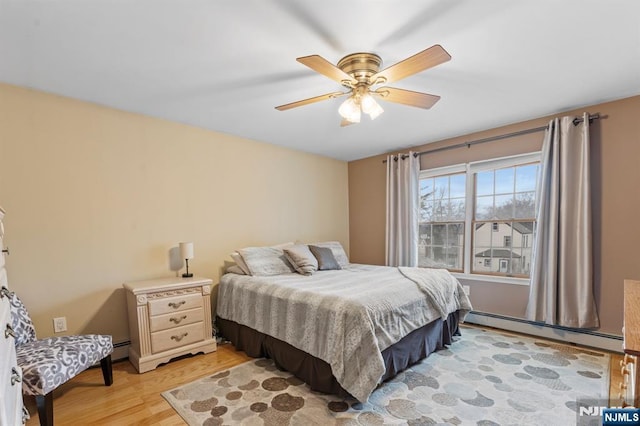 bedroom with a baseboard heating unit, light wood-style flooring, and a ceiling fan