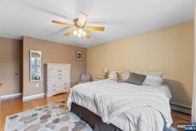 bedroom featuring baseboards, ceiling fan, baseboard heating, and wood finished floors