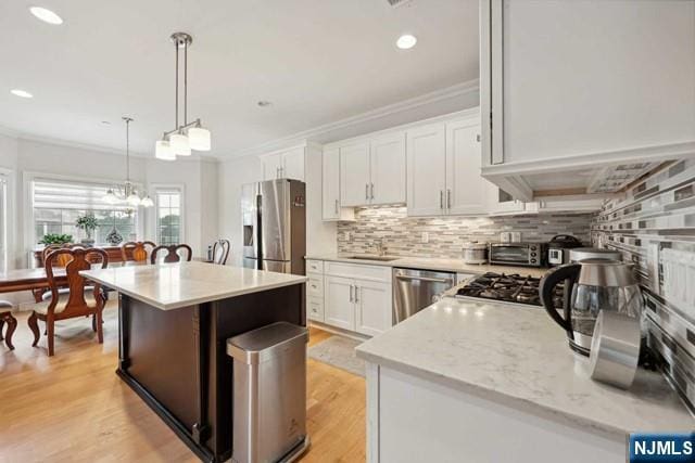 kitchen featuring tasteful backsplash, ornamental molding, stainless steel appliances, white cabinetry, and a sink