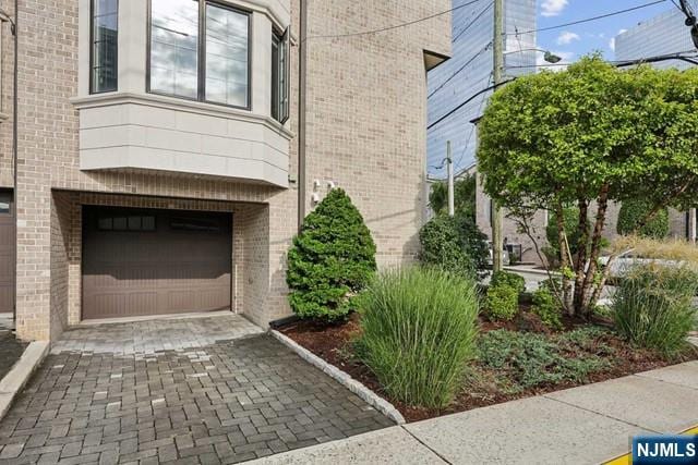 exterior space with a garage, decorative driveway, and brick siding