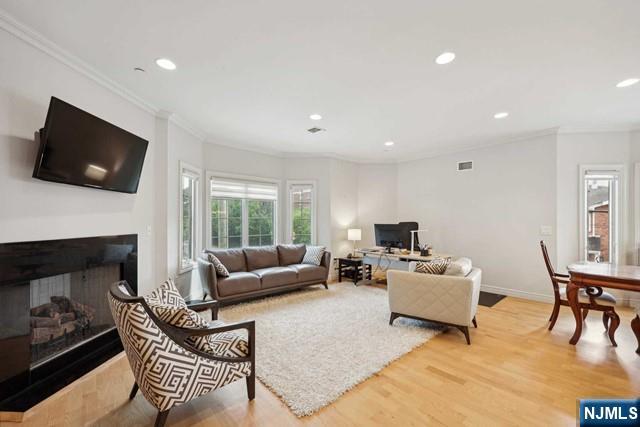 living area featuring ornamental molding, light wood-type flooring, visible vents, and recessed lighting