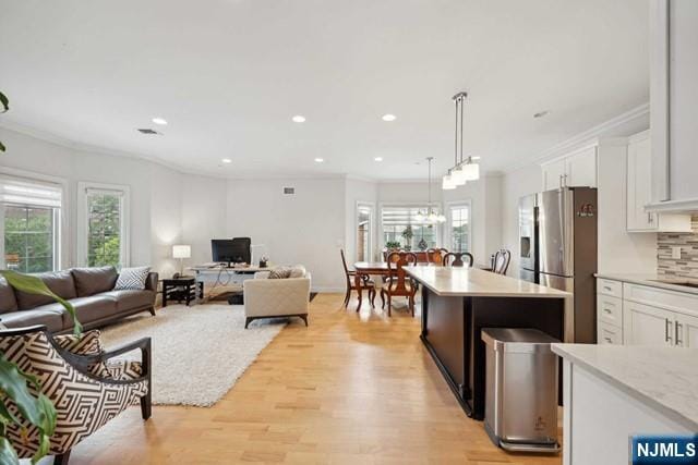 kitchen with crown molding, light wood-style flooring, backsplash, white cabinets, and stainless steel fridge