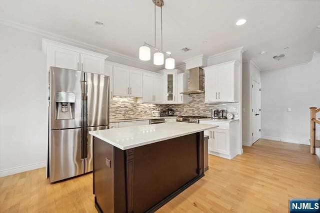 kitchen featuring white cabinetry, wall chimney range hood, a center island, tasteful backsplash, and stainless steel fridge