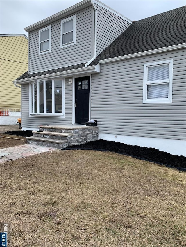 view of front facade with a front yard and roof with shingles