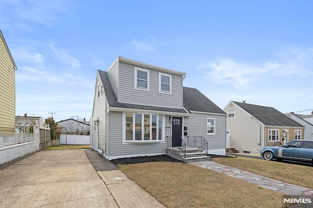 view of front of house with concrete driveway, a front lawn, roof with shingles, and fence