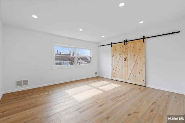 unfurnished bedroom featuring light wood finished floors, visible vents, recessed lighting, and a barn door