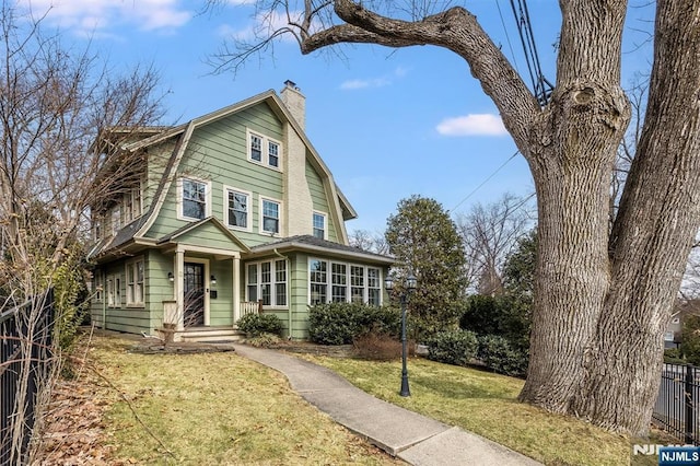 view of front of home featuring a gambrel roof, a chimney, a front yard, and fence