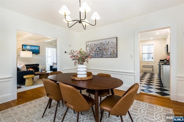 dining space featuring a notable chandelier, radiator heating unit, wood finished floors, and a lit fireplace