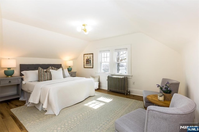 bedroom with baseboards, lofted ceiling, radiator, and wood finished floors