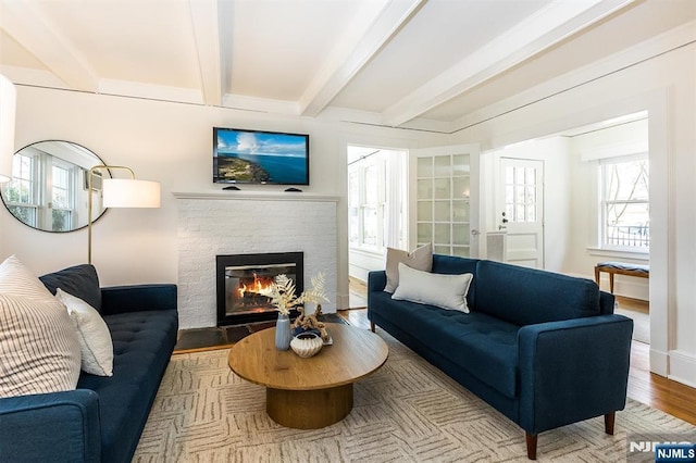 living area with a glass covered fireplace, beamed ceiling, baseboards, and wood finished floors