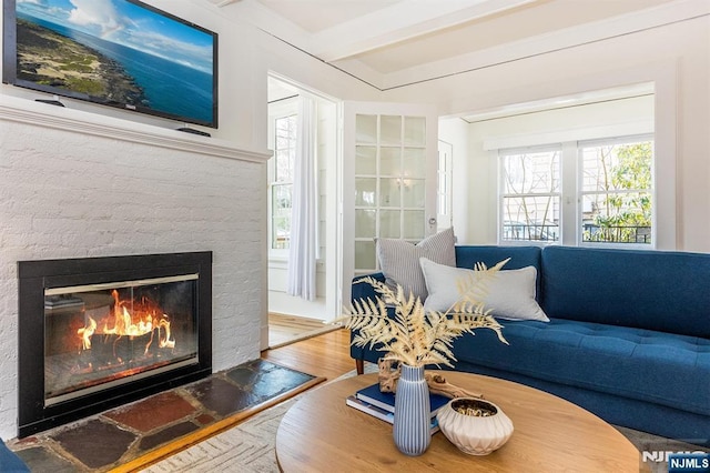 living room featuring beam ceiling, a brick fireplace, and wood finished floors