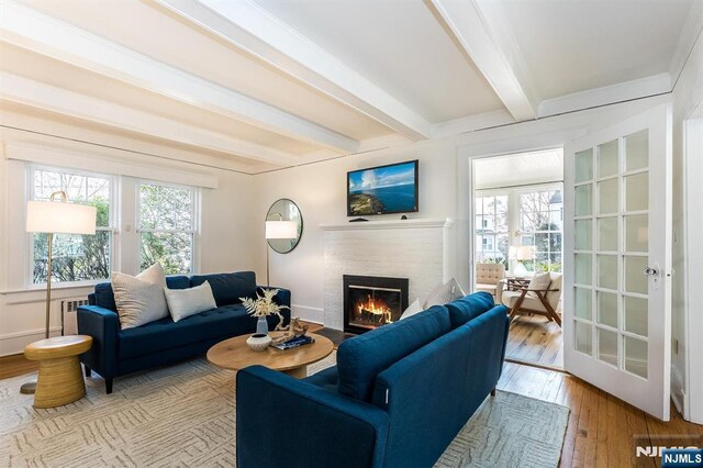 living area with baseboards, a fireplace with flush hearth, beam ceiling, and hardwood / wood-style flooring