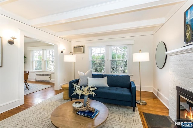 living area with a wall mounted air conditioner, radiator heating unit, beam ceiling, wood finished floors, and a glass covered fireplace