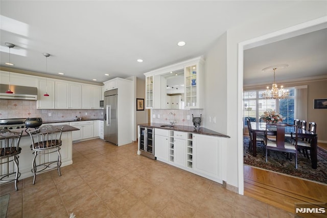 kitchen with backsplash, wine cooler, built in fridge, white cabinets, and a sink