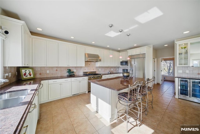 kitchen with backsplash, built in appliances, range hood, a kitchen breakfast bar, and a sink