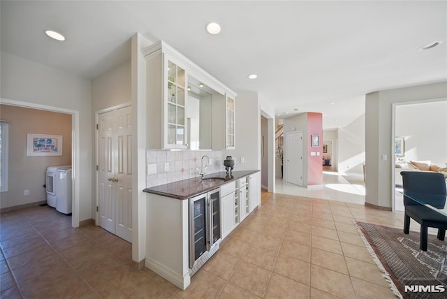 kitchen featuring a sink, backsplash, dark countertops, wine cooler, and glass insert cabinets