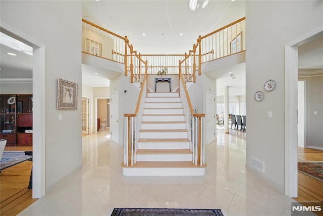 staircase with tile patterned flooring, visible vents, a high ceiling, and baseboards