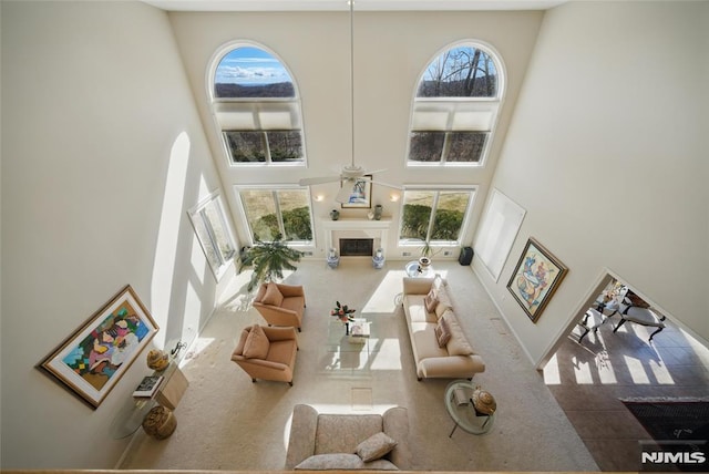 living area featuring a wealth of natural light, a glass covered fireplace, a towering ceiling, and ceiling fan