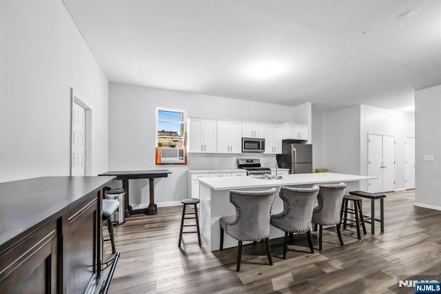 kitchen featuring a breakfast bar area, dark wood-style floors, a center island with sink, and stainless steel appliances