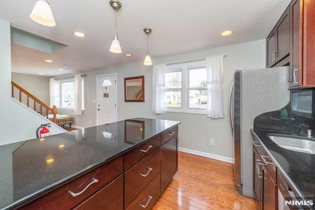 kitchen with baseboards, dark stone counters, freestanding refrigerator, decorative light fixtures, and light wood-type flooring