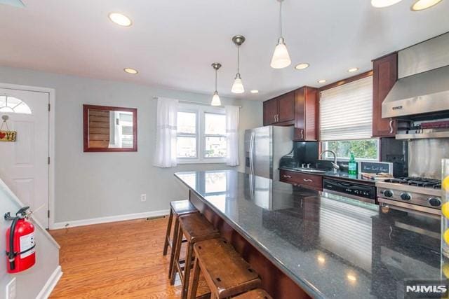 kitchen featuring a kitchen bar, light wood-style flooring, a sink, stainless steel fridge, and dishwashing machine