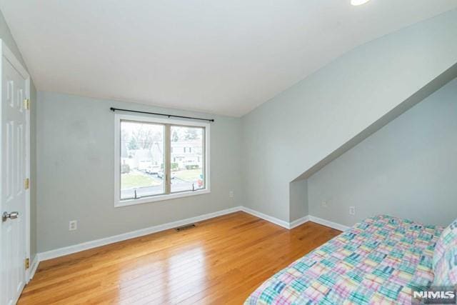 bedroom with visible vents, baseboards, light wood-style floors, and vaulted ceiling