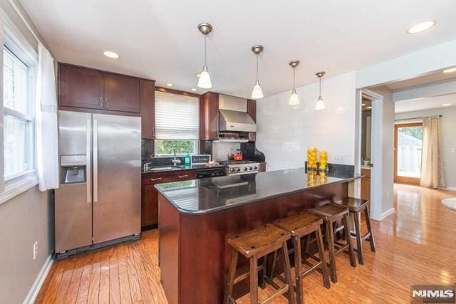 kitchen featuring a breakfast bar, dark countertops, wall chimney exhaust hood, and stainless steel fridge with ice dispenser