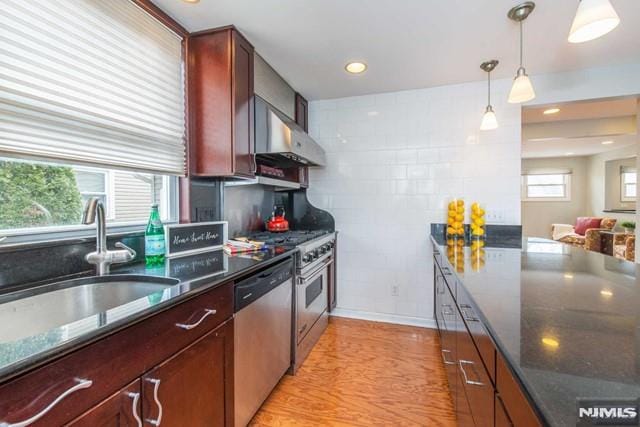 kitchen featuring a sink, recessed lighting, appliances with stainless steel finishes, wall chimney range hood, and hanging light fixtures