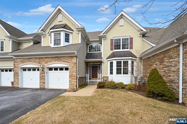 townhome / multi-family property with a standing seam roof, a shingled roof, stone siding, aphalt driveway, and metal roof