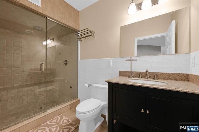 bathroom with vanity, a shower stall, tile walls, toilet, and tile patterned floors