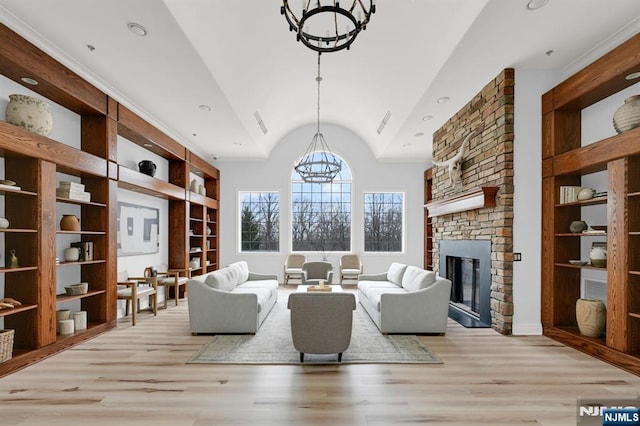 living area with built in shelves, a fireplace, vaulted ceiling, light wood-style floors, and a chandelier