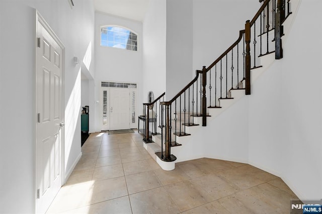 entrance foyer with light tile patterned flooring, stairway, and a towering ceiling