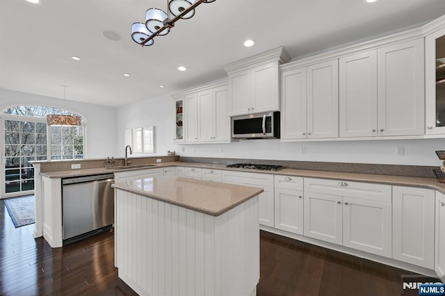 kitchen with a peninsula, stainless steel appliances, dark wood-style floors, white cabinetry, and a sink